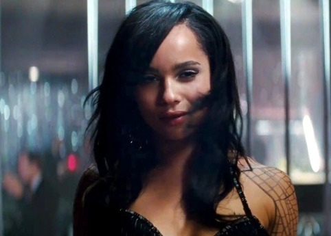 A torso shot of Zoë Kravitz - a Latina woman with brown skin and dark brown hair - in her role as Angel Salvadore. She is wearing a black halter top and smiling seductively at the camera. You can see a wing tattoo on her left arm.